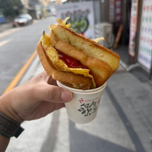 Delicious Korean street toast with egg cabbage patty, ham, and sugar in a paper cup.