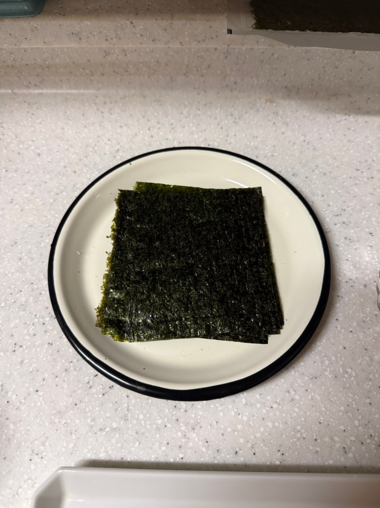 A square plate with several sheets of dark green nori seaweed placed on it.