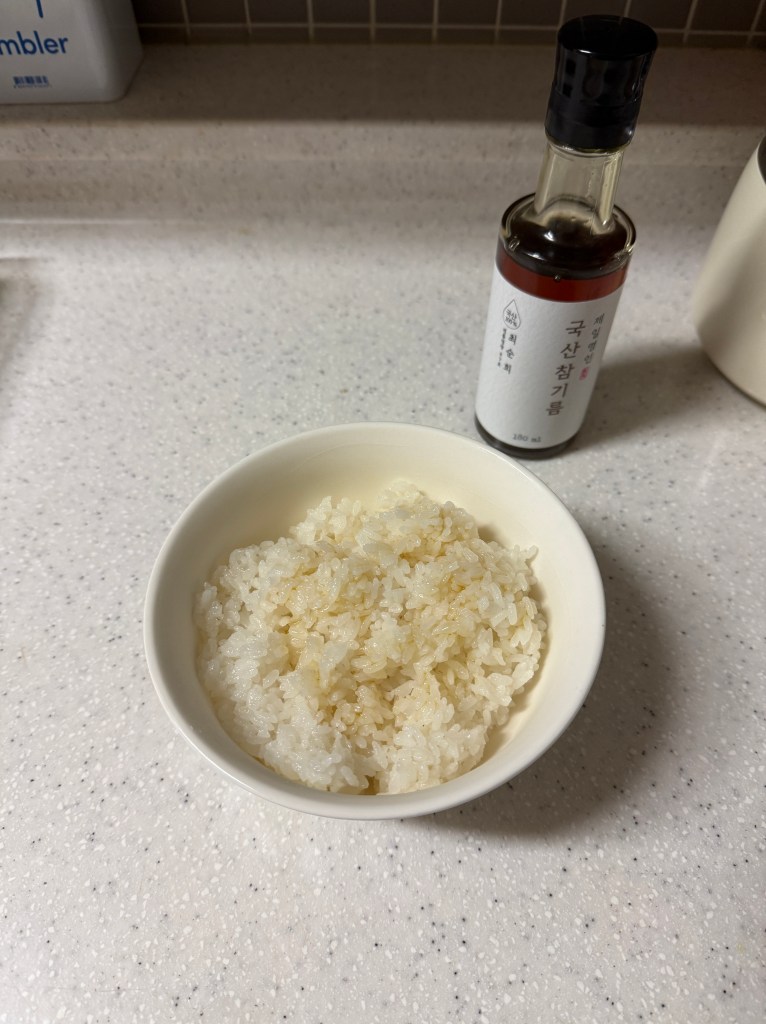 A bowl of cooked white rice next to a bottle of sauce on a kitchen countertop.