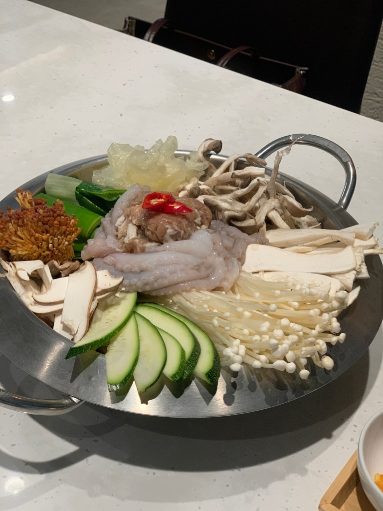 A metal plate filled with fresh seafood and various types of mushrooms and vegetables, including sliced cucumbers and garnishes.