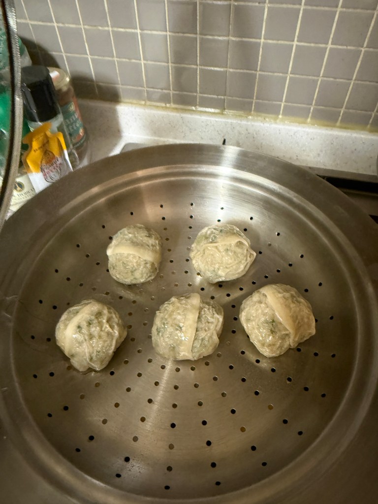 Five steamed dumplings on a metal steamer tray with small holes.