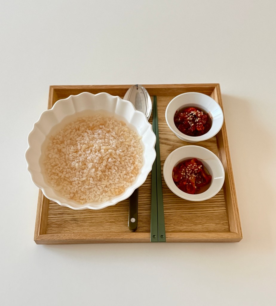 A wooden tray containing a bowl of rice, two small bowls of dipping sauces, and metal utensils.
