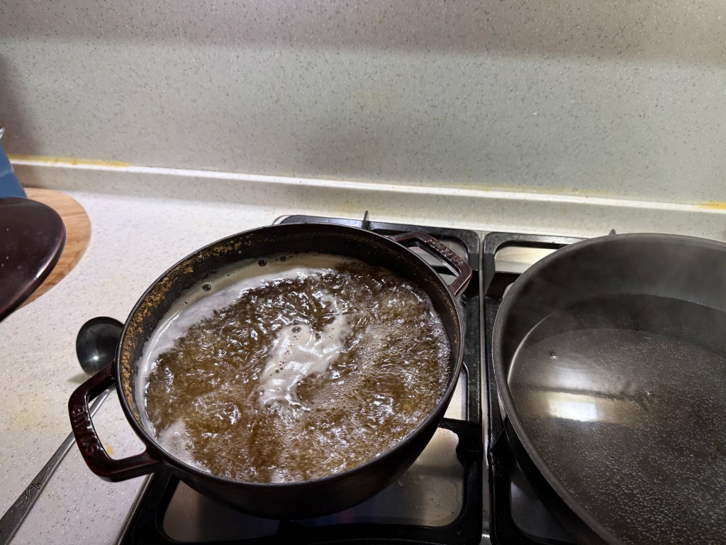 A pot of boiling water on a stove, with bubbles rising vigorously, next to a second pot with a lid.
