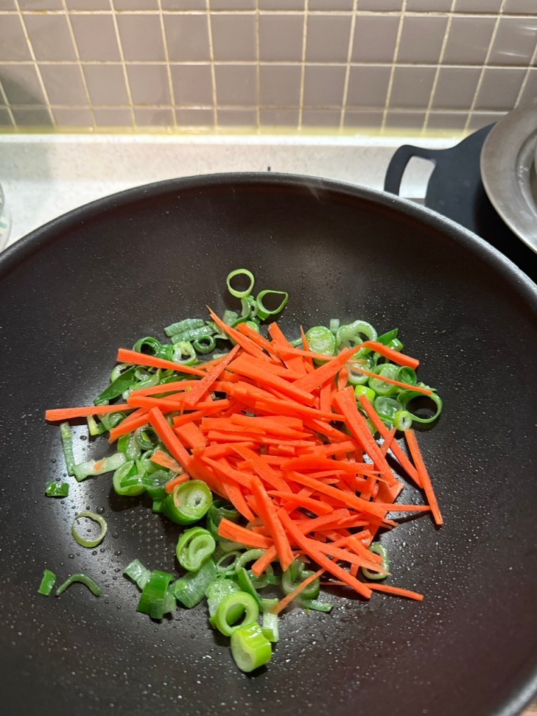 Dropping sliced onions and scallions into a heated, oiled pan.
