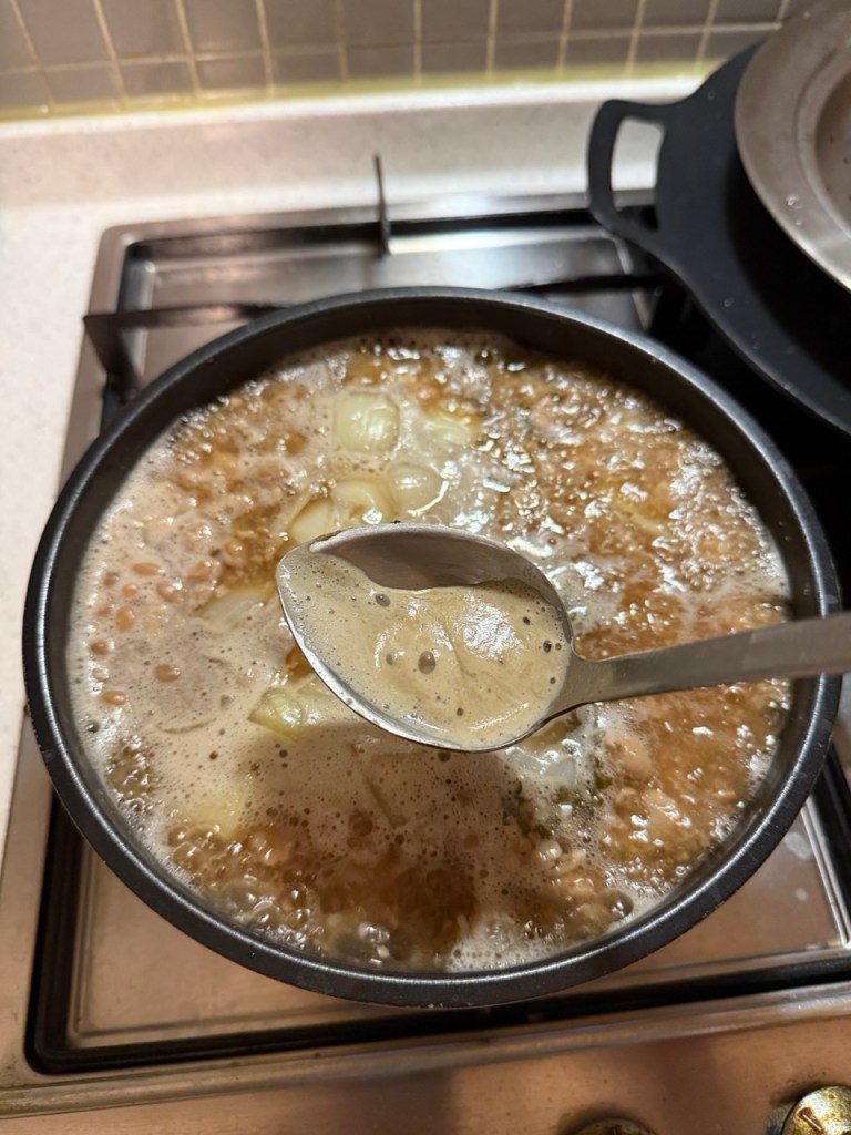 Stirring and dissolving the chunky soybean paste into the hot broth with a spoon.