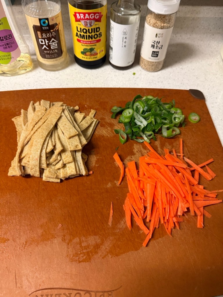 Neatly sliced strips of fish cakes on a dark wooden cutting board.