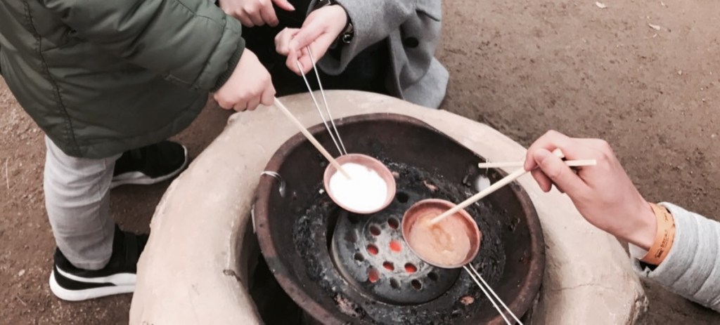 A child carefully stirring melting sugar in a small metal ladle.