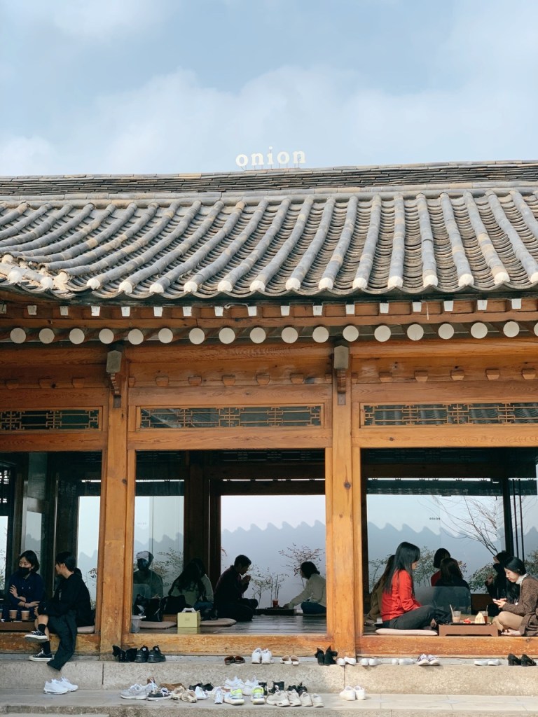 Visitors relaxing on the traditional wooden floor (Daecheongmaru) of the Hanok.