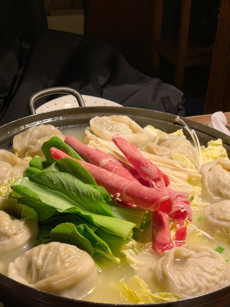 The dumpling hot pot simmering on the table, surrounded by fresh vegetables.