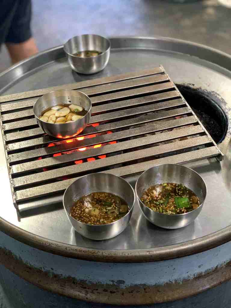 Korean BBQ being grilled on a unique drum can grill in a standing restaurant.