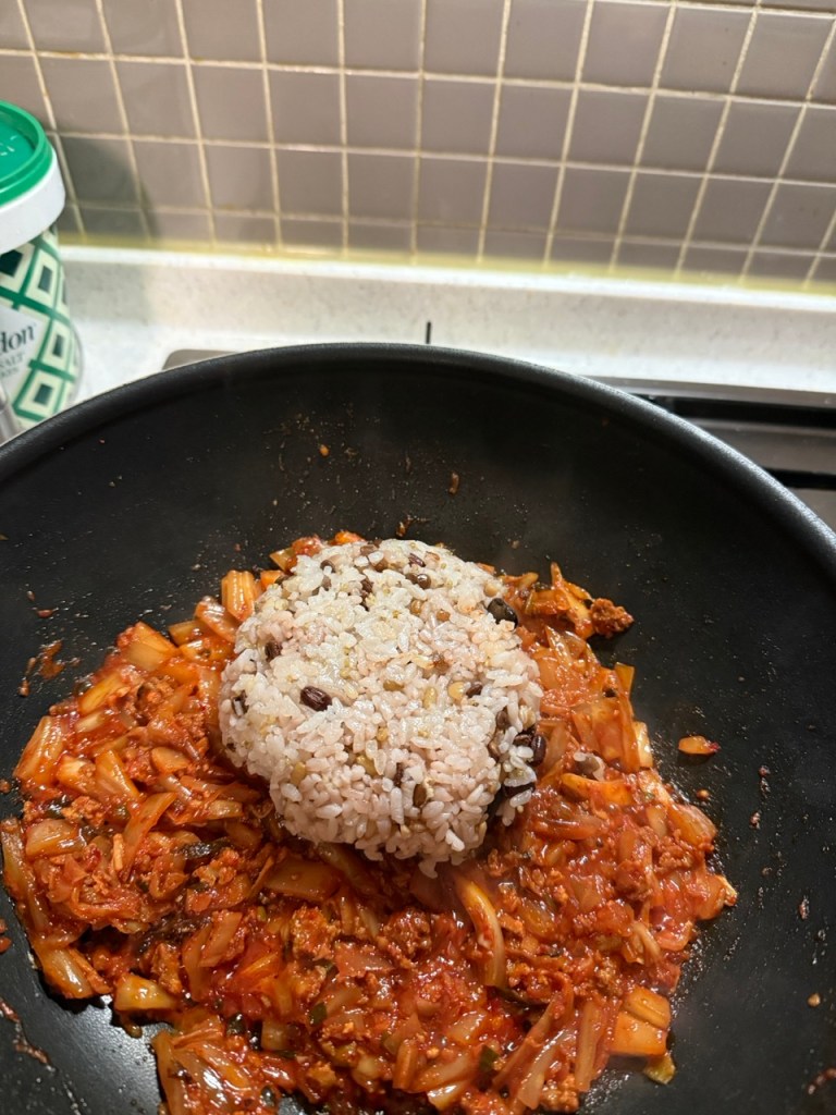 Mixing white rice with the seasoned stir-fried Kimchi until evenly coated.