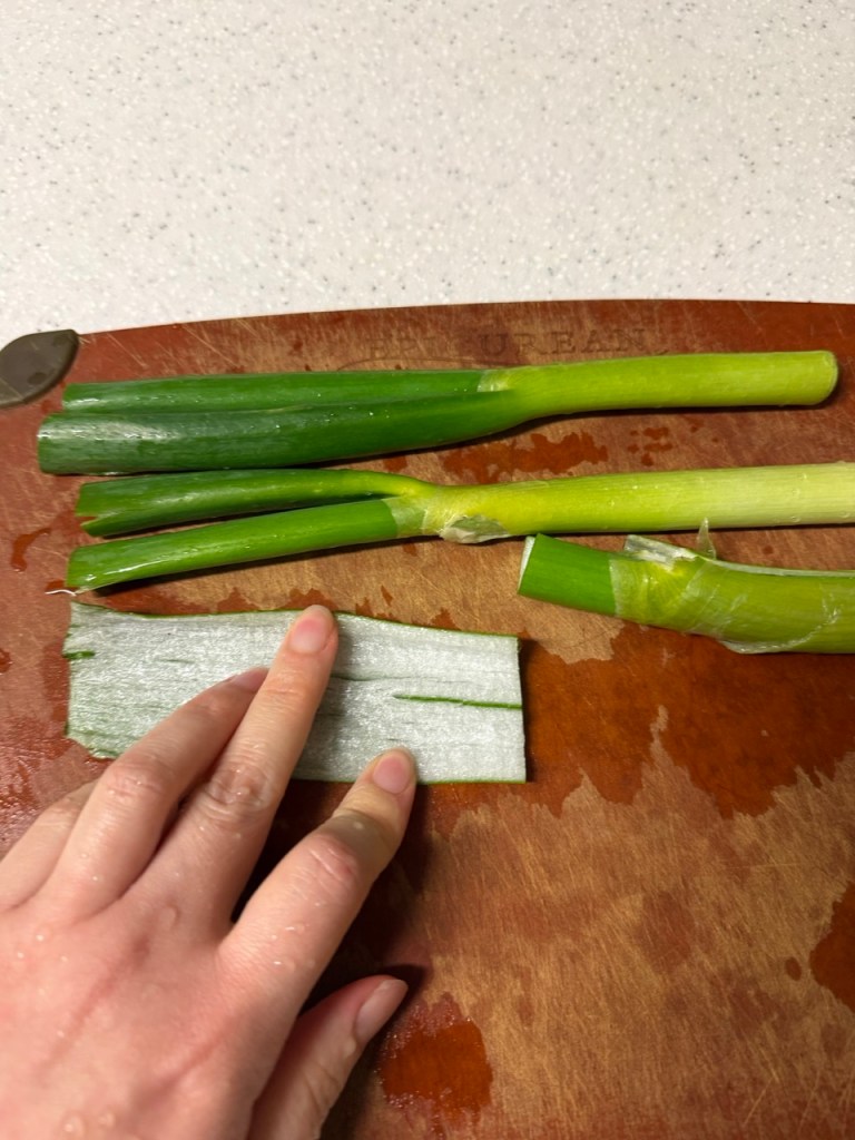 Thinly shredding green onions into long strips using a knife or a green onion slicer.