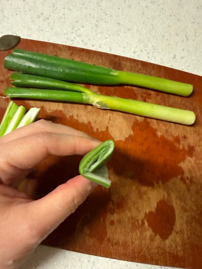 Thinly shredding green onions into long strips using a knife or a green onion slicer.