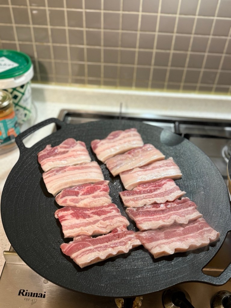 Sizzling thick slices of pork belly (Samgyeopsal) being grilled on a home electric pan.