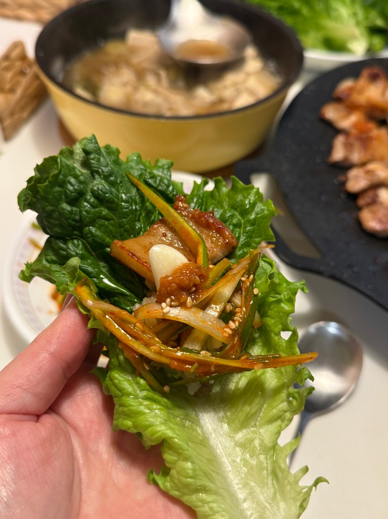 A fresh lettuce wrap (Ssam) with grilled pork belly, ssamjang sauce, and a garlic clove.