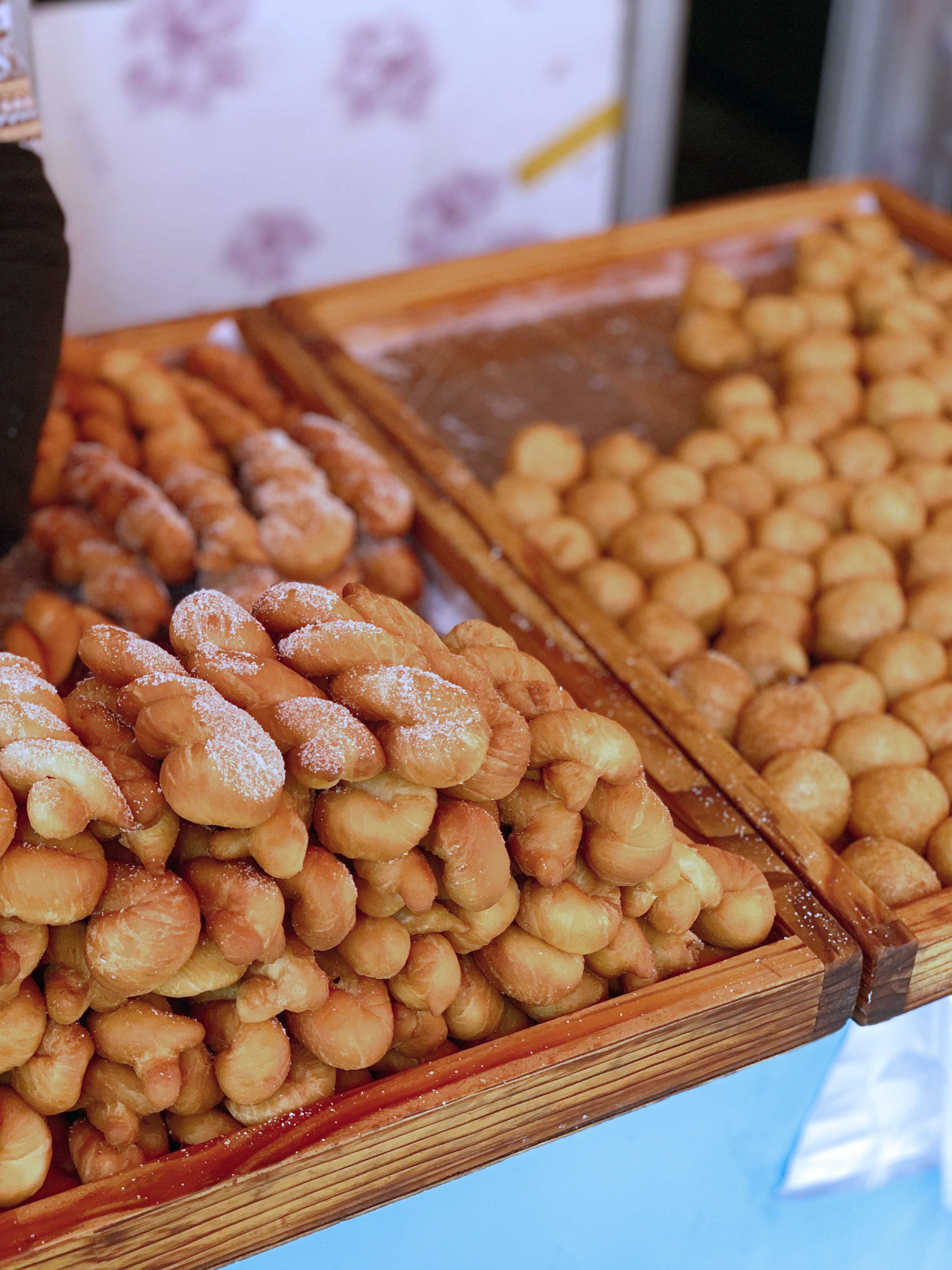 A pile of freshly fried, golden-brown twisted doughnuts coated in sugar.