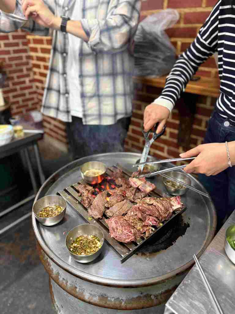 Close-up of meat sizzling and cooking over hot charcoal on a metal grill.