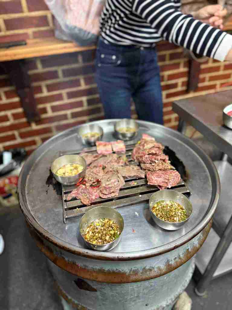 Close-up of meat sizzling and cooking over hot charcoal on a metal grill.