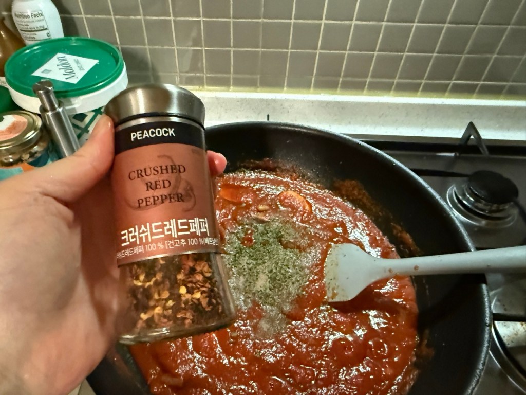 Adding some of crushed red pepper to the pan with sautéed ingredients.
