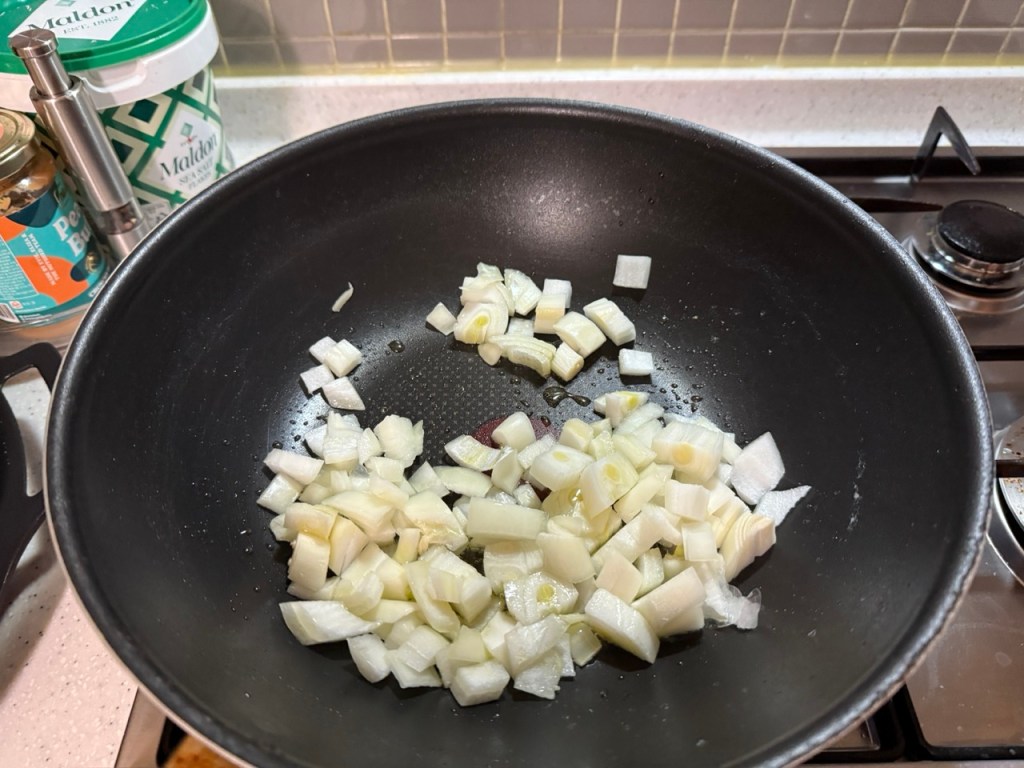 Stir-frying sliced sausages, onions, and bell peppers in a hot pan.