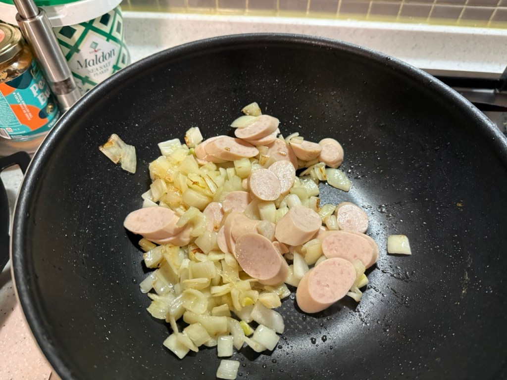 Stir-frying sliced sausages, onions, and bell peppers in a hot pan.