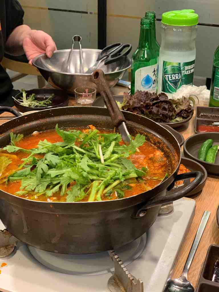 A steaming pot of spicy fish stew with octopus and various vegetables.
