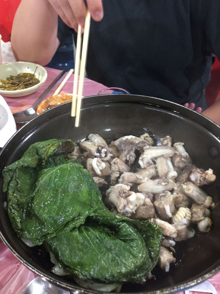 Sizzling salt-grilled hagfish with whole garlic cloves and onions on a grill.