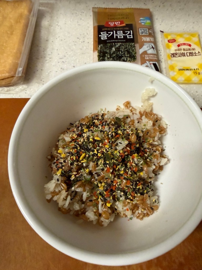 Mixing warm white rice with sweet vinegar and vegetable flakes in a glass bowl.