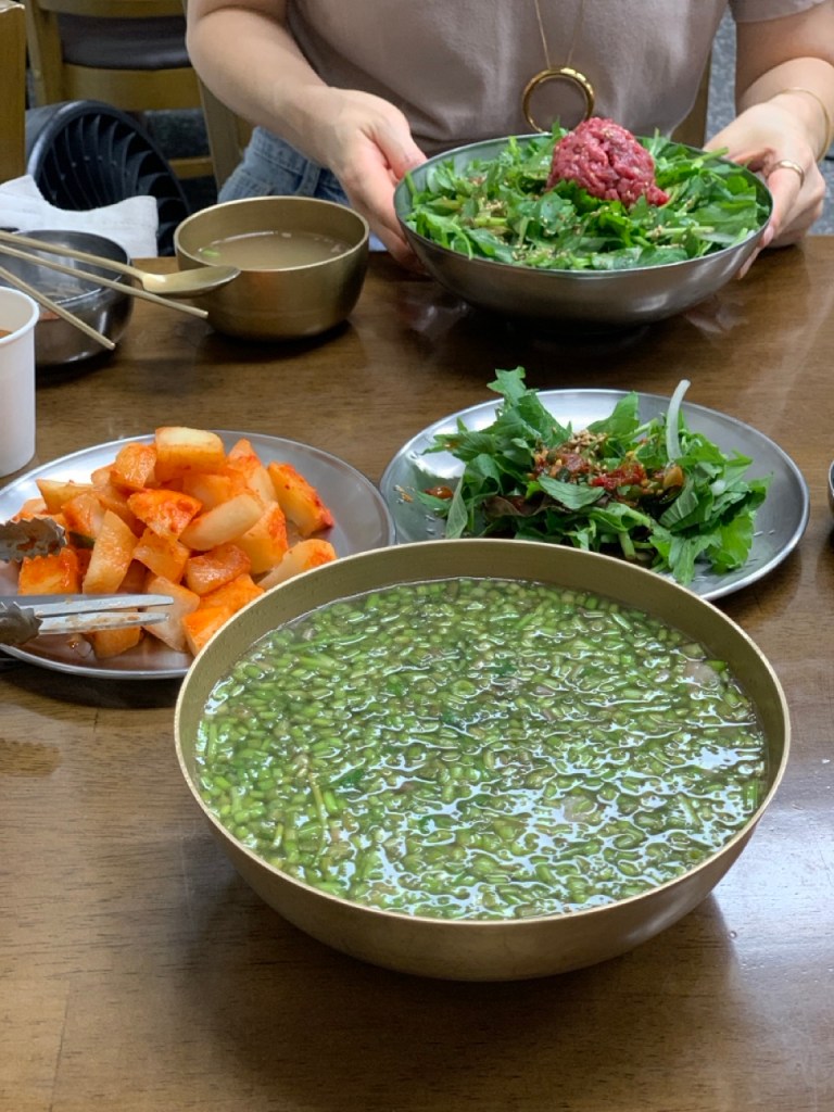 A clear beef soup topped with a vibrant green layer of fresh water parsley.