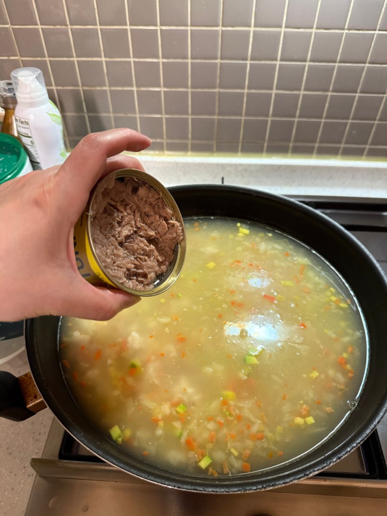 Adding canned tuna into the pot to simmer for a savory flavor.