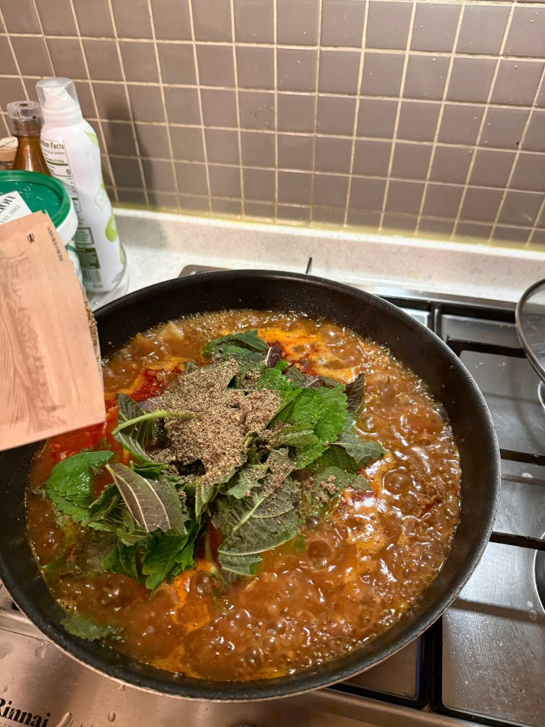 Scooping a generous amount of nutty perilla seed powder into the stew for that authentic restaurant-style Gamjatang flavor.