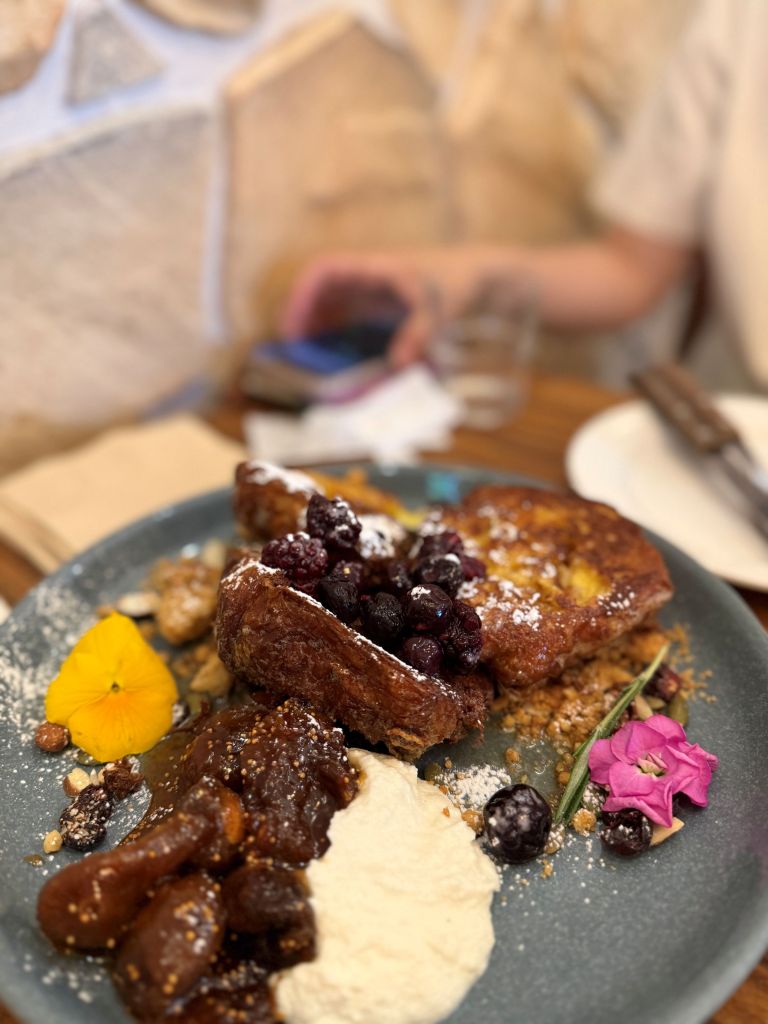 A thick, caramelized, and ultra-fluffy French toast topped with fresh seasonal berries and maple syrup at Cafe OATT.