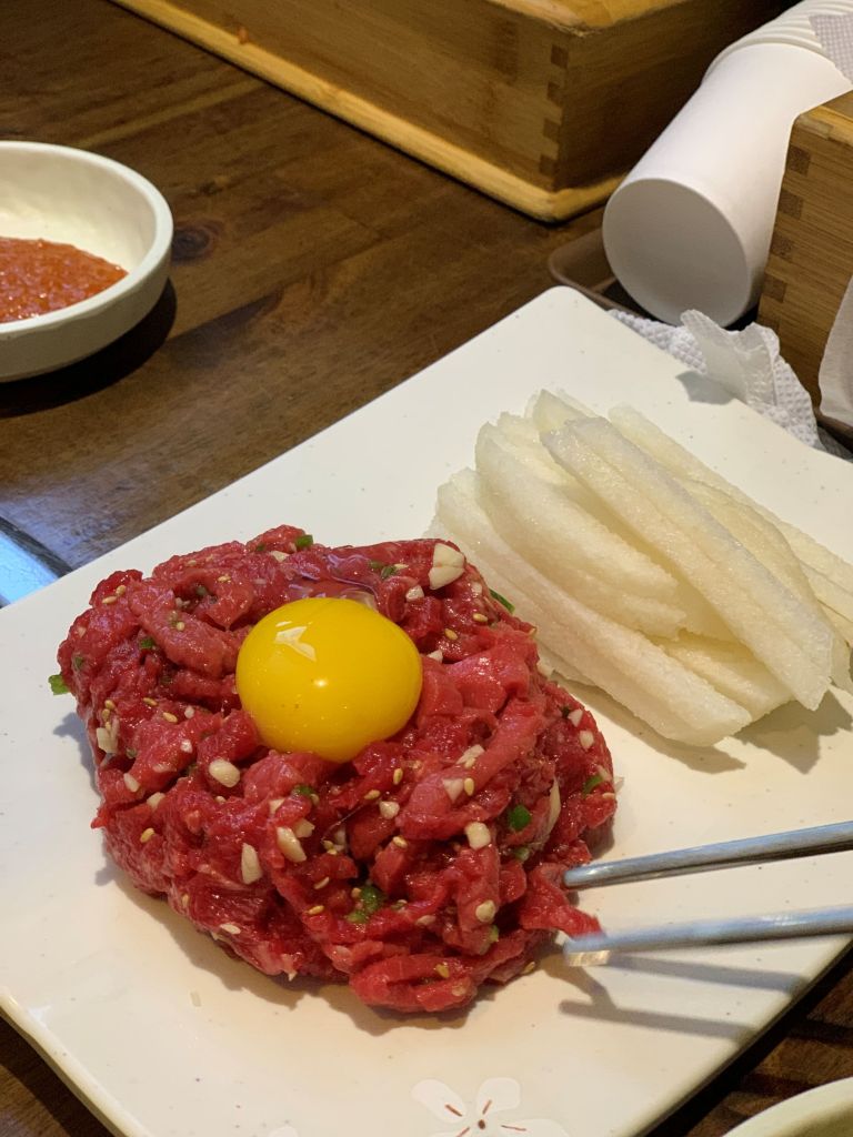 A gourmet plate of seasoned raw Korean beef tartare (Yukhoe) topped with a glossy raw egg yolk, served with crisp sweet pear slices.