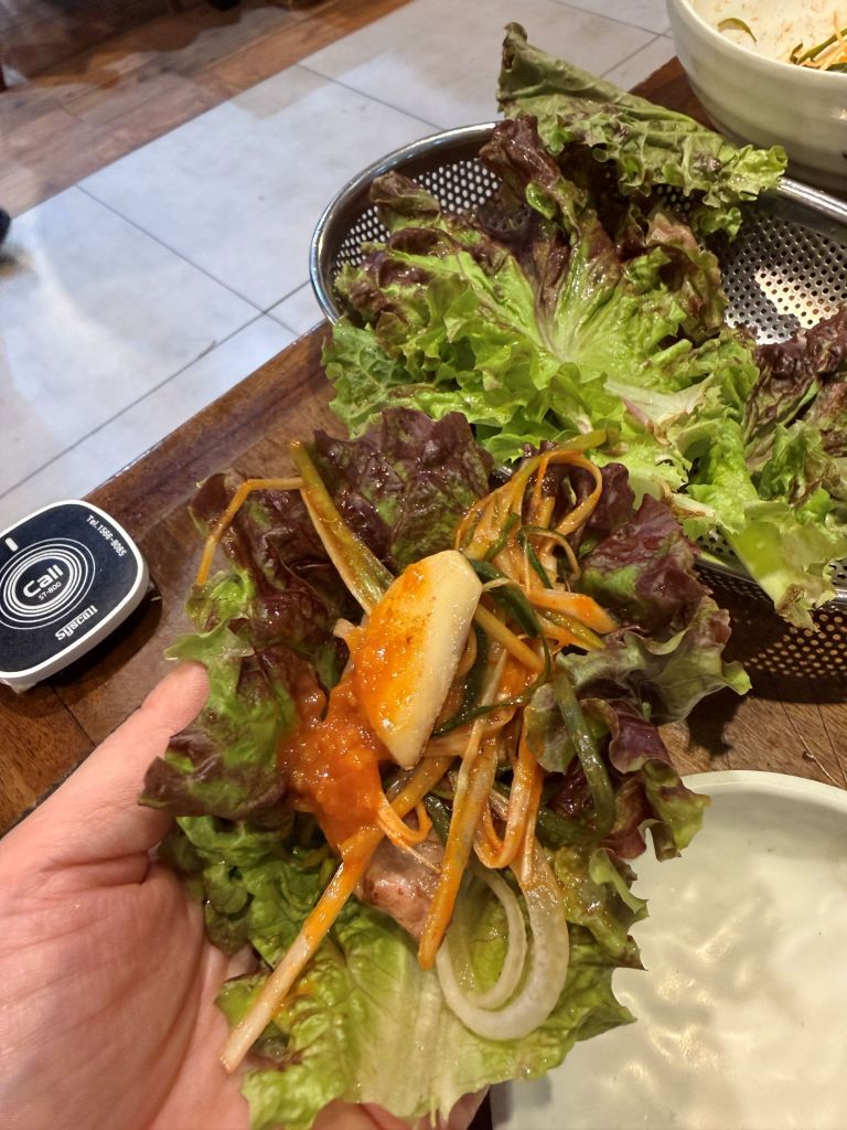 Adding a perfectly blistered clove of roasted garlic and a dollop of savory, fermented ssamjang paste onto a Samgyeopsal wrap.