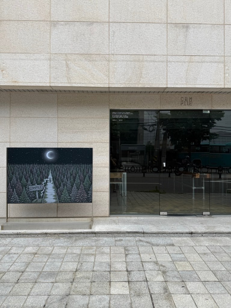 The sleek, minimalist metal and glass exterior facade of Compile cafe, a quiet hidden gem in Hongdae.