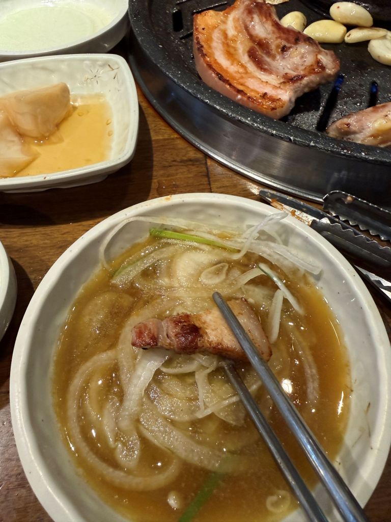 A succulent slice of grilled Samgyeopsal topped with crunchy, tangy soy-marinated onions, balancing the rich pork fat.