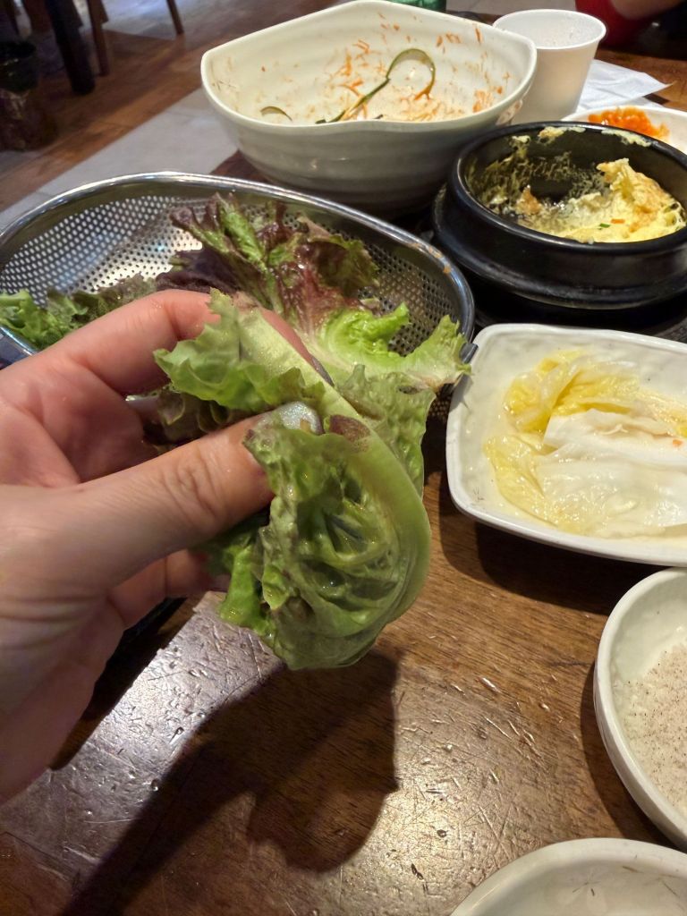 Demonstrating the traditional Korean dining etiquette of folding a ssam wrap into a compact, single-bite pouch.