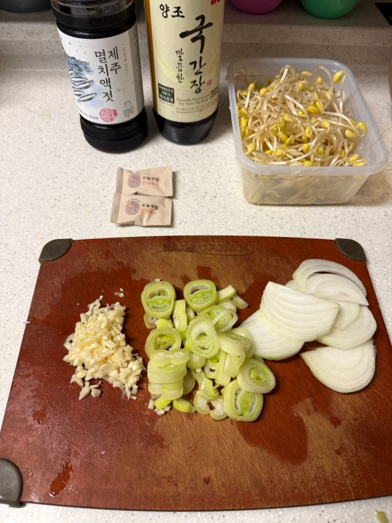 A fresh and clean ingredient display for Kongnamul-guk, featuring crisp soybean sprouts, sliced scallions, garlic, and red chili peppers.