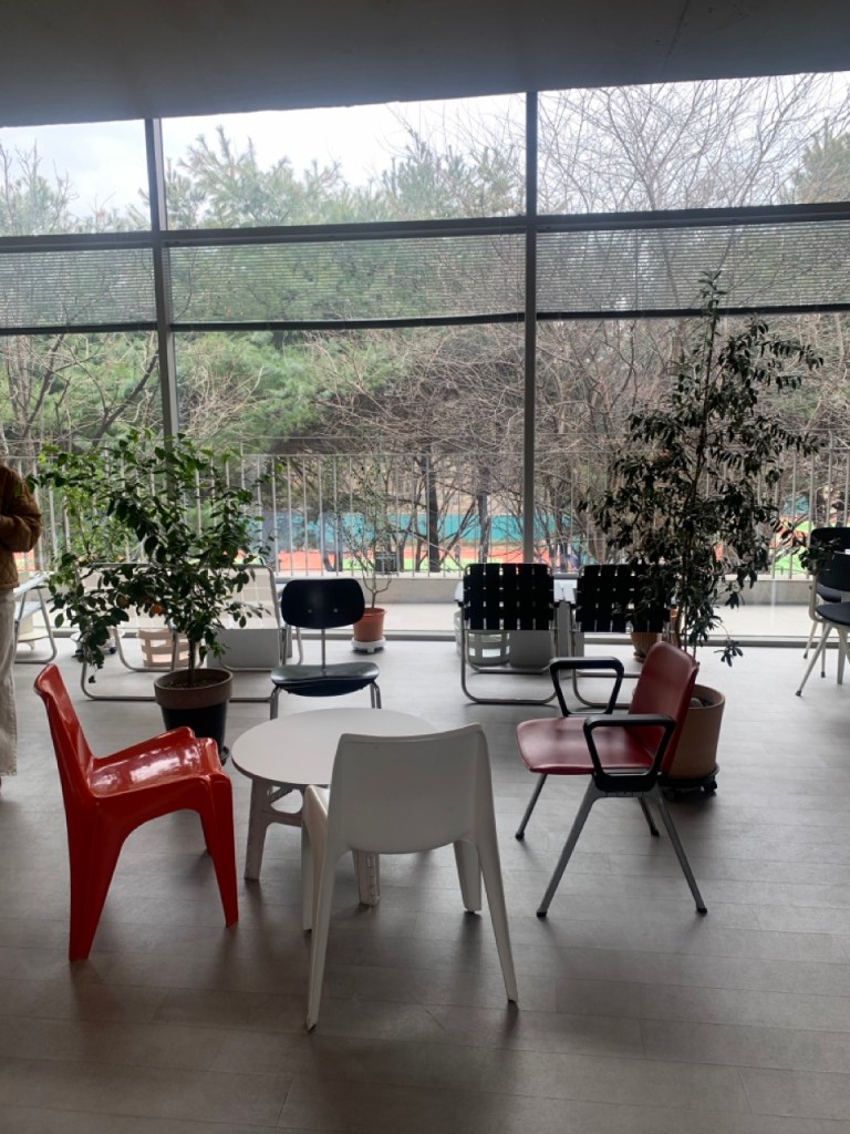 A breathtaking cinematic shot of the massive glass window at PLAD cafe, framing a gorgeous panoramic view of the lush green Seoul Forest.