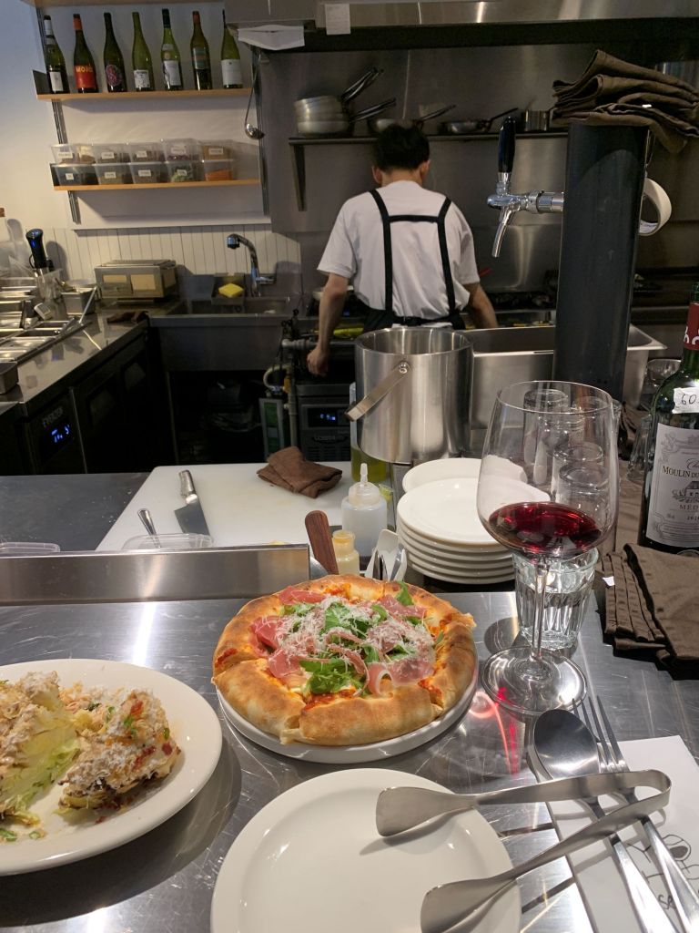 A romantic and warm-lit dinner table spread at Yoho, showcasing the steak, pizza, and signature salad paired with wine.