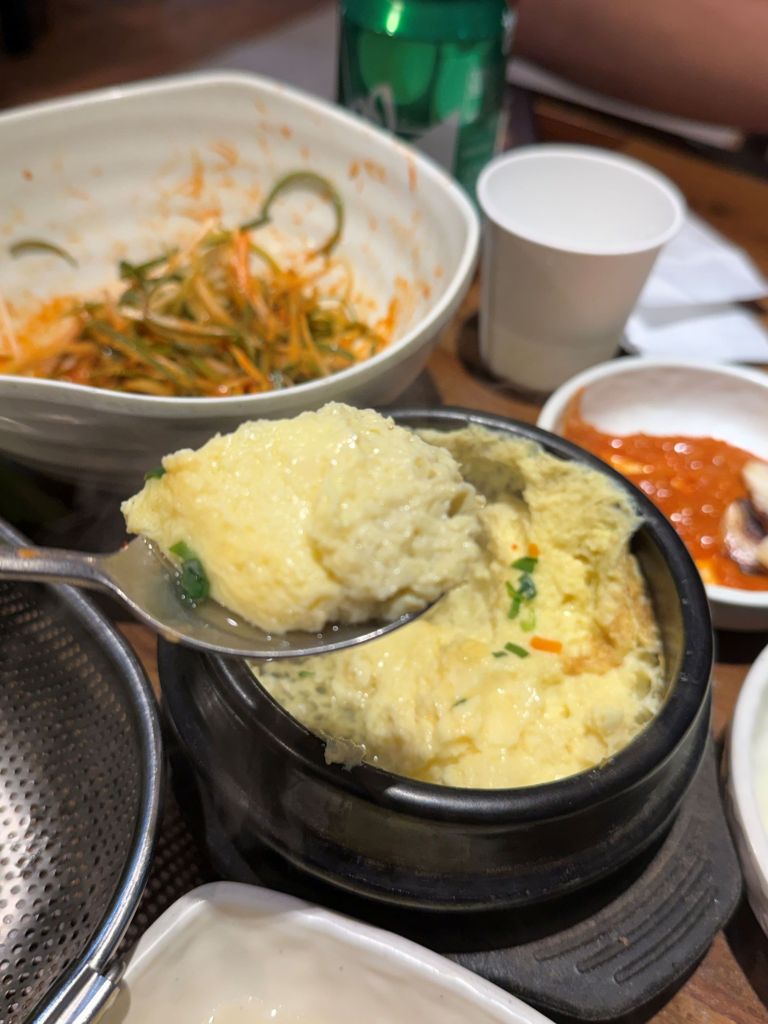 Scooping a generous portion of steaming, pillow-soft, and savory egg custard directly from the bubbling pot.