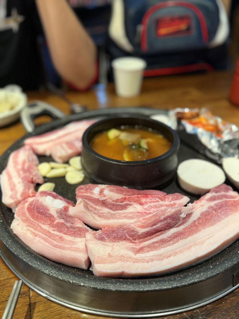 Thick-cut, juicy slices of pork belly neatly arranged in a perfect ring around the central boiling stew on a hot griddle.