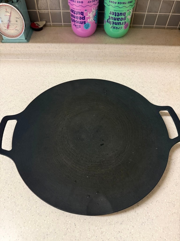 A high-satisfaction close-up showing a deep concave cast iron griddle pan designed for collecting savory meat oil.