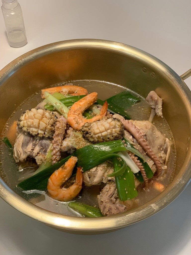 A magnificent top-down view of Haeshintang, the ultimate premium summer wellness stew featuring a whole chicken loaded with fresh octopus and abalones.