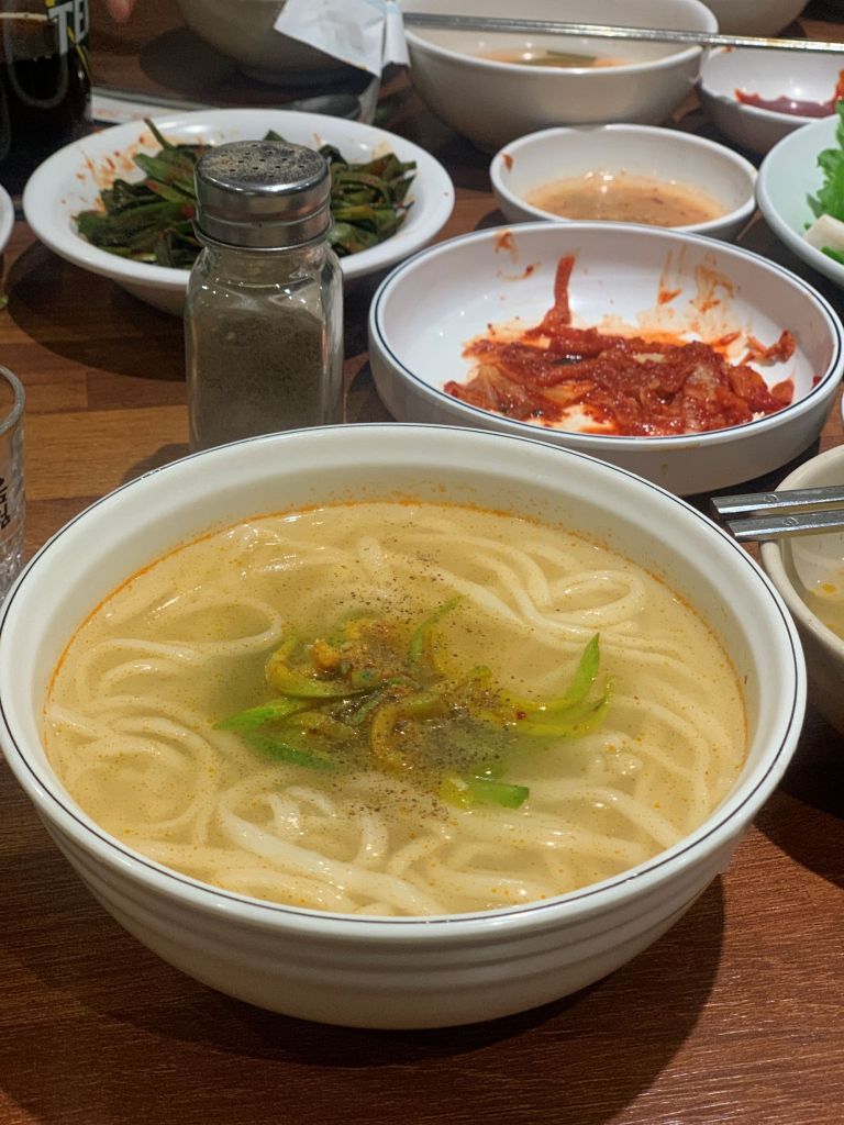 A refined top-down view of the signature clear beef broth kalguksu, thin-cut chopped noodles, at Hanseong Kalguksu in Nonhyeon-dong.
