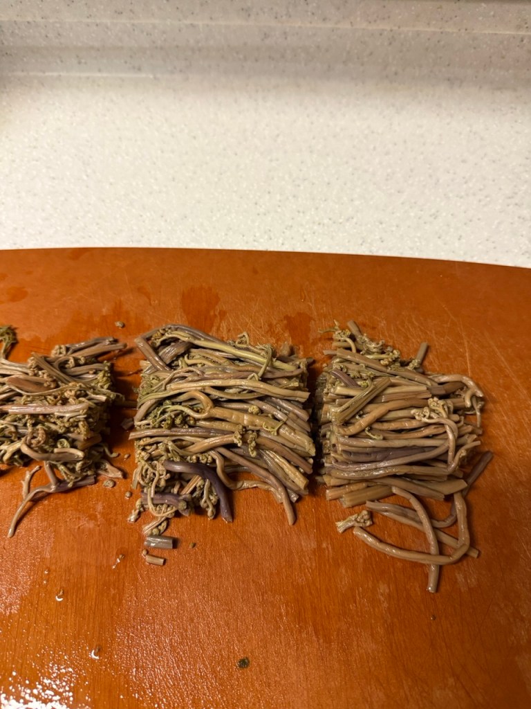 A high-satisfaction top-down shot of neatly chopped, tender boiled bracken fern (gosari) lined up uniformly on a wooden cutting board.