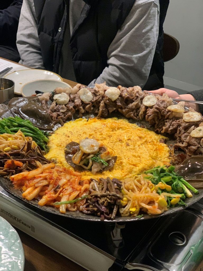 A professional server pouring liquid egg crust around the outer rim of the Korean beef brisket platter.