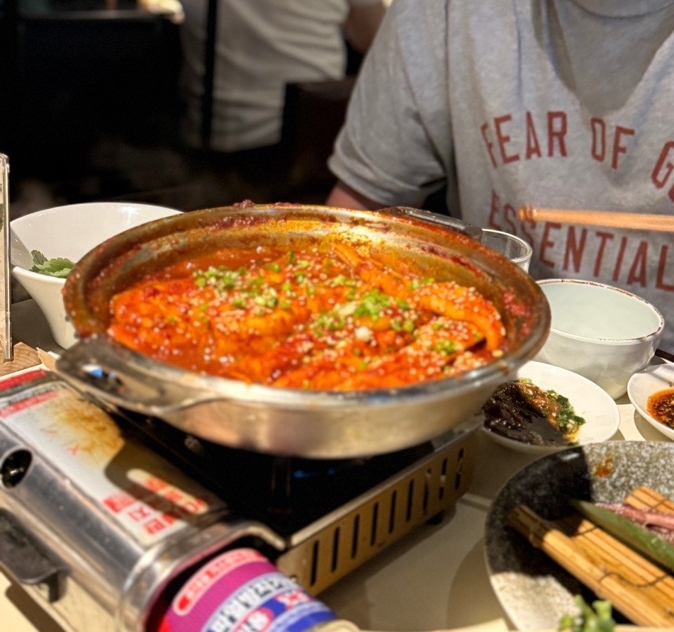 A cinematic focus on a shallow pot of spicy Korean braised fish simmering with deeply seasoned radish slices.