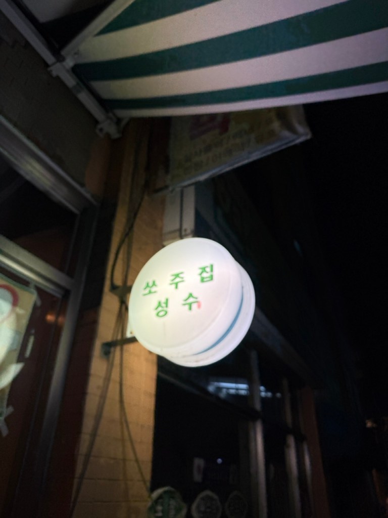 The iconic, bright minimalist retro-style white and red signboard of Ssojujip lighting up the Seongsu alley.