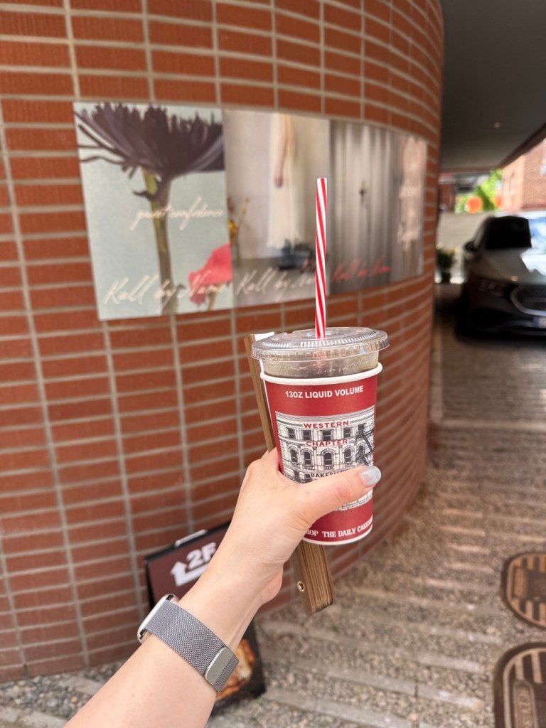 A high-satisfaction focus on a stylish to-go coffee cup held against the rustic wooden storefront of Western Chapter.